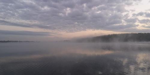 a misty lake with a cloudy sky and some trees at Haus auf dem See Elise, Matheo, Mads, und Jarle in Ferchesar