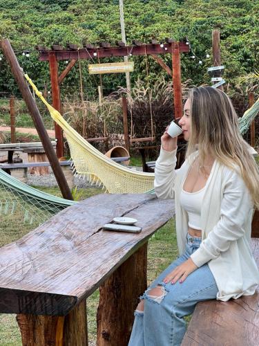 a woman sitting on a bench drinking a cup of coffee at Recanto dos Pássaros in Alto Caparao