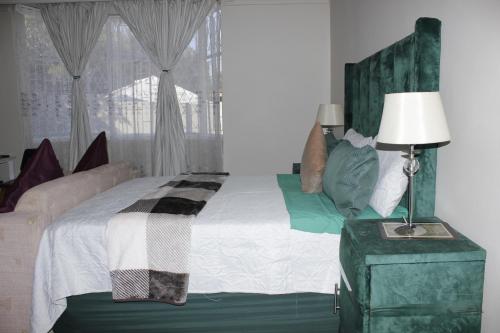 a bedroom with a bed and a lamp and a window at DreamWest Living The Guesthouse in Krugersdorp