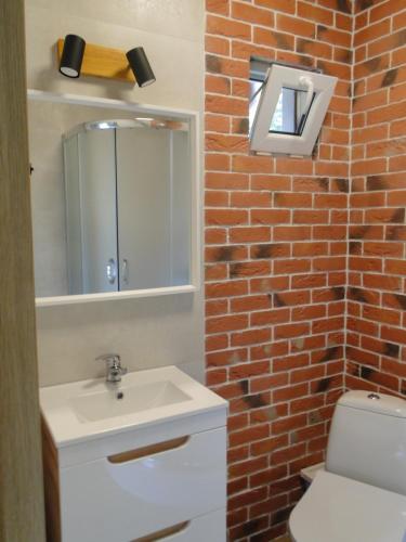 a bathroom with a white sink and a brick wall at Domki Zielona Osada in Szczenurze
