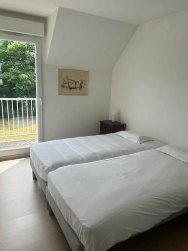 deux lits dans une chambre blanche avec une fenêtre dans l'établissement L escapade du Cap, à Barneville-Carteret