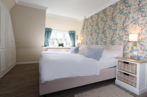 a bedroom with a large white bed with a floral wallpaper at Boutiquehotel Seiler Hof Keitum in Keitum