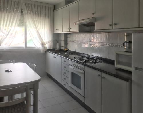 cocina con armarios blancos, fogones y mesa en 3 bedrooms apartement at Laxe 80 m away from the beach with balcony, en Laxe
