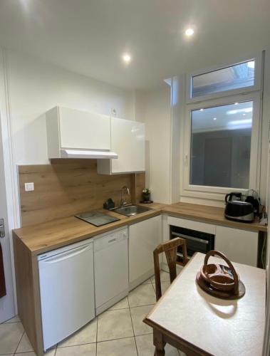 une cuisine avec des armoires blanches, une table et une fenêtre dans l'établissement Meublés d'Anna, à Aix-les-Bains