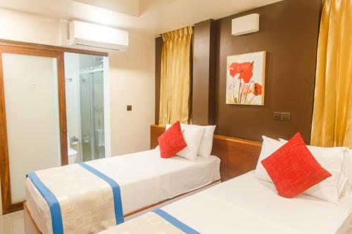 two beds in a hotel room with red and white pillows at Club Blu in Male City