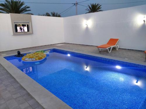 ein blauer Swimmingpool mit einem Stuhl neben einer weißen Wand in der Unterkunft Villa LELLA HADHERYA in Taguermess