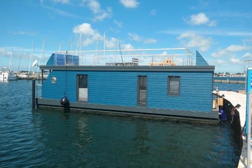 a blue house boat sitting on the water at Hausboot Kaddi`s SunDREAM - Huus & Meer in Fehmarn
