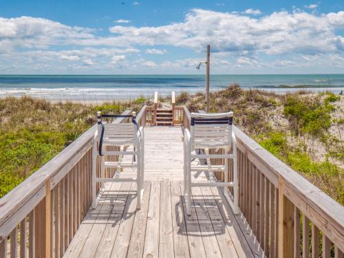 two chairs on a wooden walkway to the beach at A Charm of Finches in Surf City