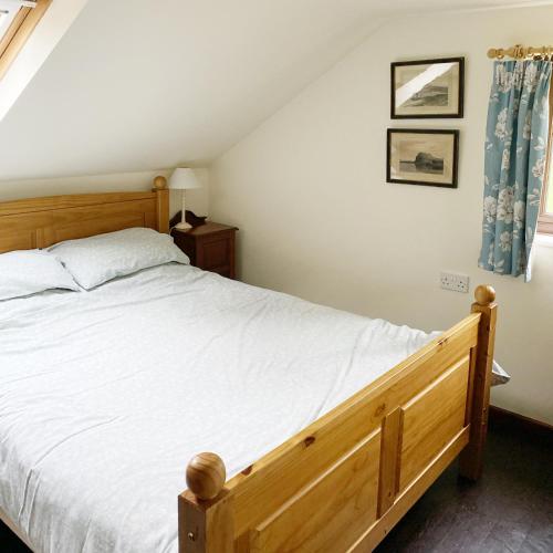a bedroom with a wooden bed with white sheets at Llynhillyn Cottage in Presteigne