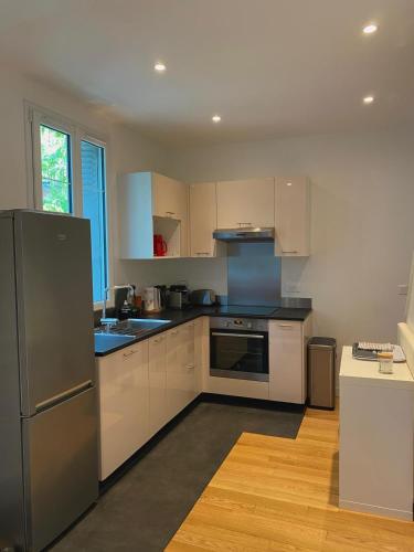 une cuisine avec des armoires blanches et un réfrigérateur en acier inoxydable dans l'établissement Maison avec jardin située à 15mn de Paris centre, à Créteil