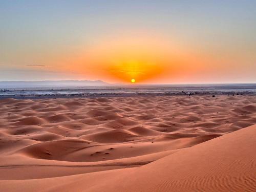 a desert with the sun setting in the horizon at Blue Sky Luxury Camp in Merzouga