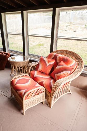 a wicker chair and stool in a room with windows at Catskills Retro Retreat- Upstate Home W Hot Tub in Saugerties