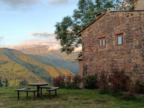 a table and benches in front of a stone building at La cabaña mirador de los Valles Pasiegos in Vega de Pas