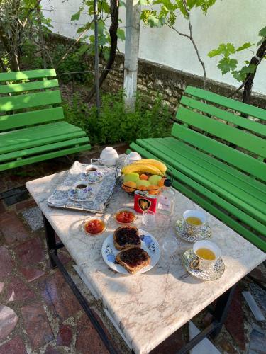 a table with food and fruit on it with two green benches at Vila Nea in Berat