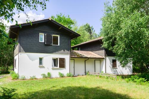une grande maison blanche avec un toit noir dans l'établissement La Cachette du Lac Un cocon nature pour des souvenirs inoubliables, à Lacanau