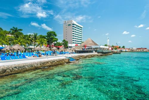 a beach with chairs and umbrellas in the water at El Cid La Ceiba Beach in Cozumel