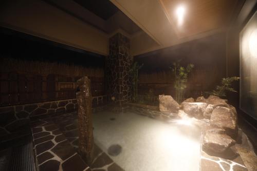 a hot tub in a room with a stone wall at Dormy Inn Maebashi in Maebashi