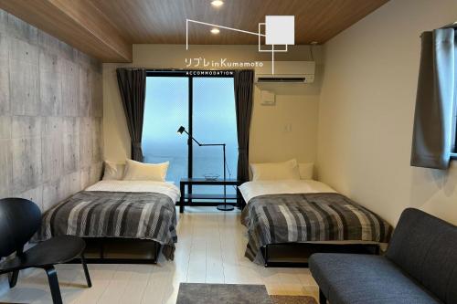 two beds in a room with a window and a couch at リブレ in Kumamoto 302 in Kumamoto