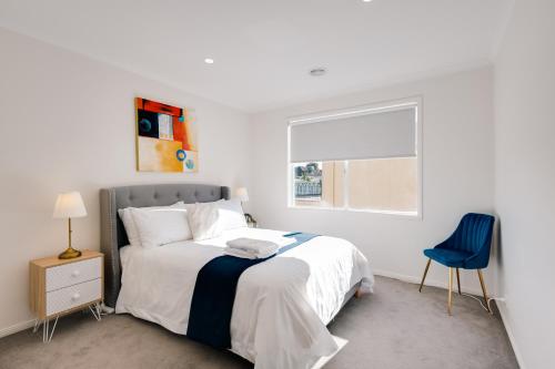 a white bedroom with a bed and a blue chair at StayAU Family Group 6BR Oasis Sanctuary Lakeview in Point Cook