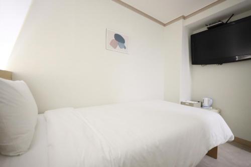 a bedroom with a white bed and a flat screen tv at J5 Hostel in Seoul