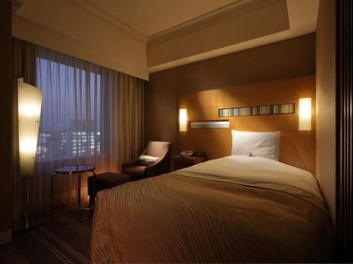 福岡市にあるホテルオークラ福岡のベッド1台、椅子、窓が備わる客室です。
