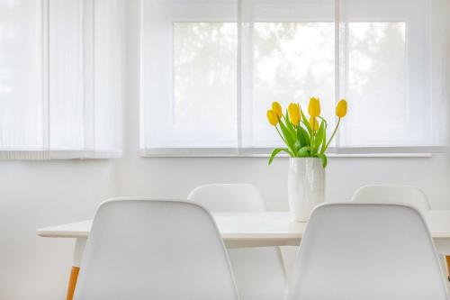 a white dining room with white chairs and a table with yellow tulips at Anchor Apartman by HelloBalatonlelle in Balatonlelle