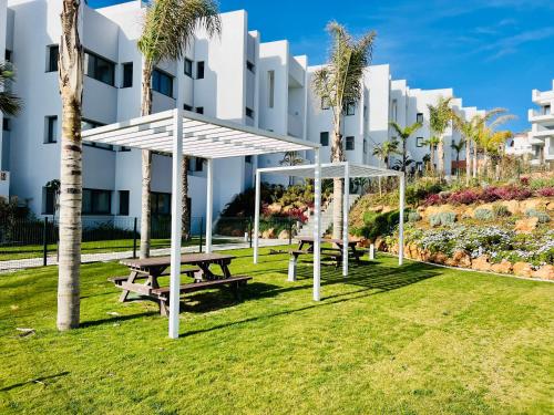 a picnic table and benches in front of a building at Logement moderne et cosy avec piscine, jacuzzi, salle de sport et billard in Estepona