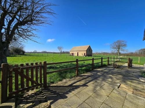 a wooden fence next to a field with a barn at Ancien gîte de chasse, calme & nature in Saint-Michel-Tubœuf