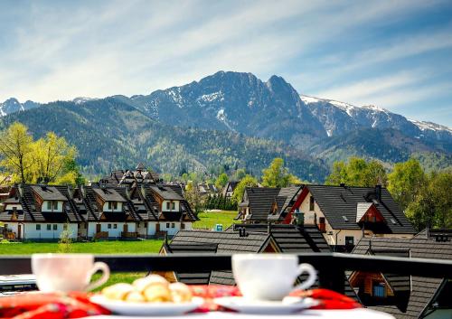 a table with plates of food on a balcony with mountains at Grand Podhale Resort&Spa Zakopane - Jacuzzi - Sauna fińska i Łaźnia parowa - Widok na Tatry in Zakopane