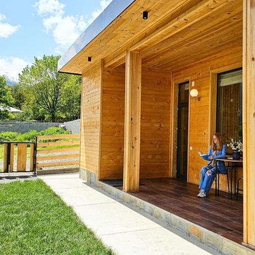 a woman sitting on the porch of a wooden house at Mountain-view double villa, pet-friendly, ideal for long stays Svaneti Countryside 3 in Mestia