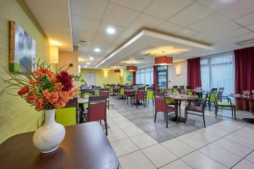 un restaurant avec des tables et des chaises et un vase fleuri dans l'établissement Residence Seniors Les Essentielles, à Caen