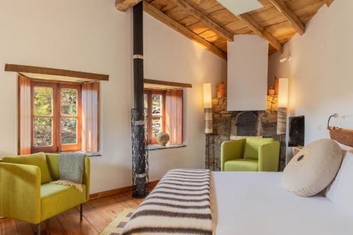 a bedroom with a bed and two green chairs at Cerdeira - Home for Creativity in Lousã
