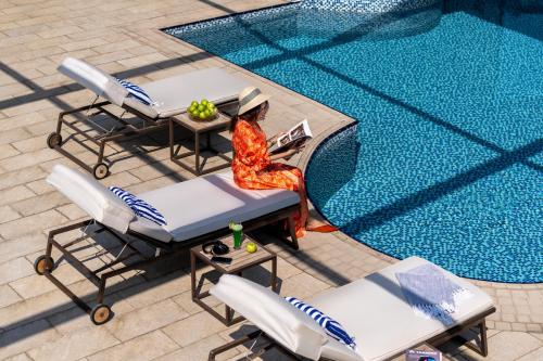 a woman sitting on a chair next to a swimming pool at Novotel Jeddah Tahlia in Jeddah