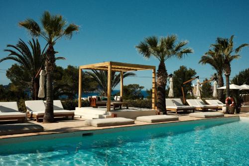 a swimming pool with lounge chairs and palm trees at Petunia Ibiza, a Beaumier hotel in Cala Vadella