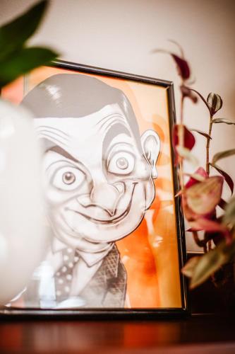 a drawing of a man in a frame next to a plant at Lost At Sea in Sarandë