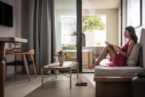 a woman sitting on a couch reading a book at VAYA Suites by Omilos Hotels in Amoudara Herakliou
