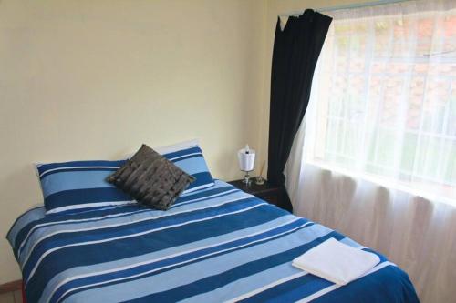 a bedroom with a blue and white striped bed with a window at Ezulwini Zululami in Ezulwini