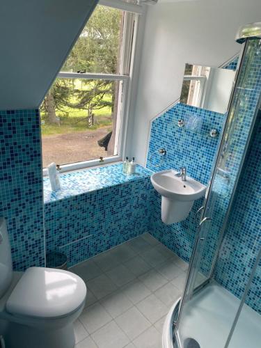 a blue tiled bathroom with a shower and a sink at Glenan Lodge Self Catering in Tomatin
