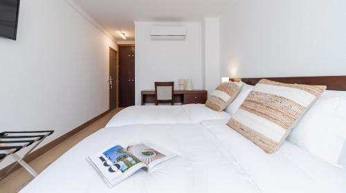 a bedroom with a white bed with a book on it at Albergaria Quim Barreiros in Vila Praia de Âncora
