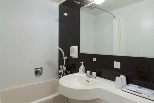 La salle de bains est pourvue d'un lavabo, d'une baignoire et d'un miroir. dans l'établissement Comfort Hotel Kurosaki, à Kitakyūshū