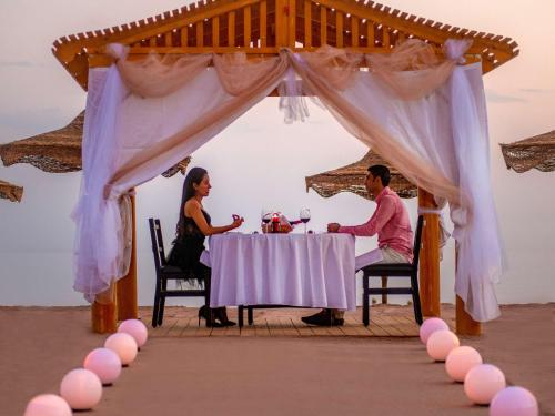 Movenpick Taba Resort & Spa في طابا: رجل وامرأة يجلسان على طاولة تحت مظلة