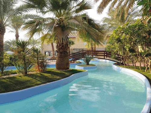 a swimming pool with palm trees in a resort at Montrose - A Mayfair Collection Hotel in Kuwait