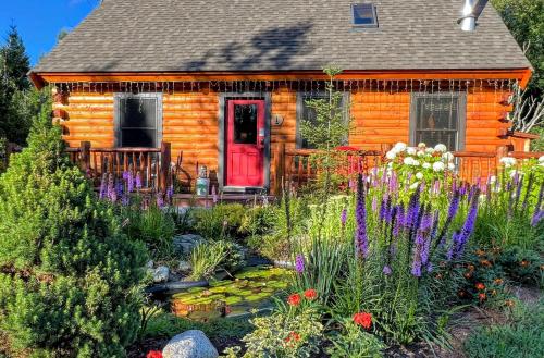 a house with a red door and a garden with flowers at BC Log cabin with private beach river fire pit AC wifi onsite trails ski slope views in Carroll