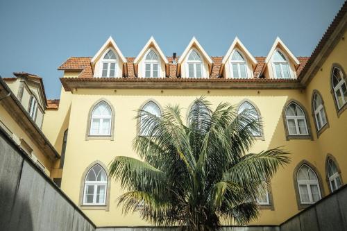 a yellow building with a palm tree in front of it at Vilar Oporto Hotel in Porto