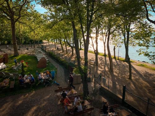 people sitting on benches in a park near the water at Hotel Anna Villa in Balatonföldvár