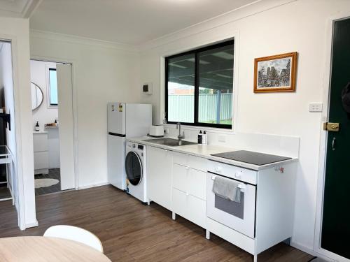 Una cocina blanca con fregadero y refrigerador. en Bowerbird Cottage, en Camberwarra