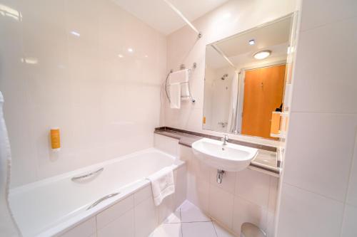 uma casa de banho branca com um lavatório e uma banheira em Premier Inn Abu Dhabi Airport Business Park em Abu Dhabi