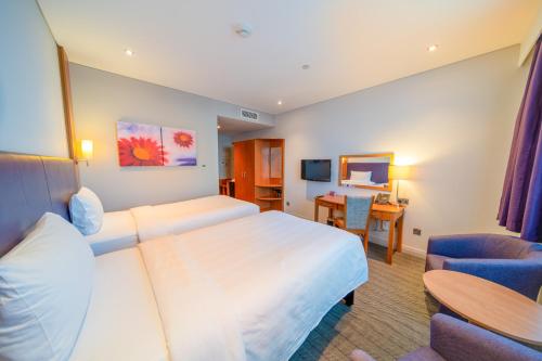 a hotel room with two beds and a desk at Premier Inn Abu Dhabi Airport Business Park in Abu Dhabi