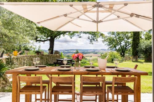 a wooden table and chairs under a white umbrella at Le Mas Gascon - Maison de vacances 4 étoiles avec piscine et vue proche de Lectoure in Marsolan