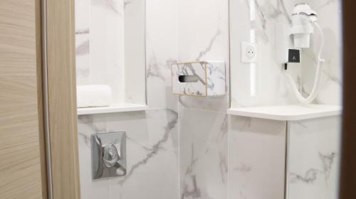 - une salle de bains avec des murs en marbre blanc et un téléphone dans l'établissement Geographotel Paris-Roissy CDG Airport, au Mesnil-Amelot